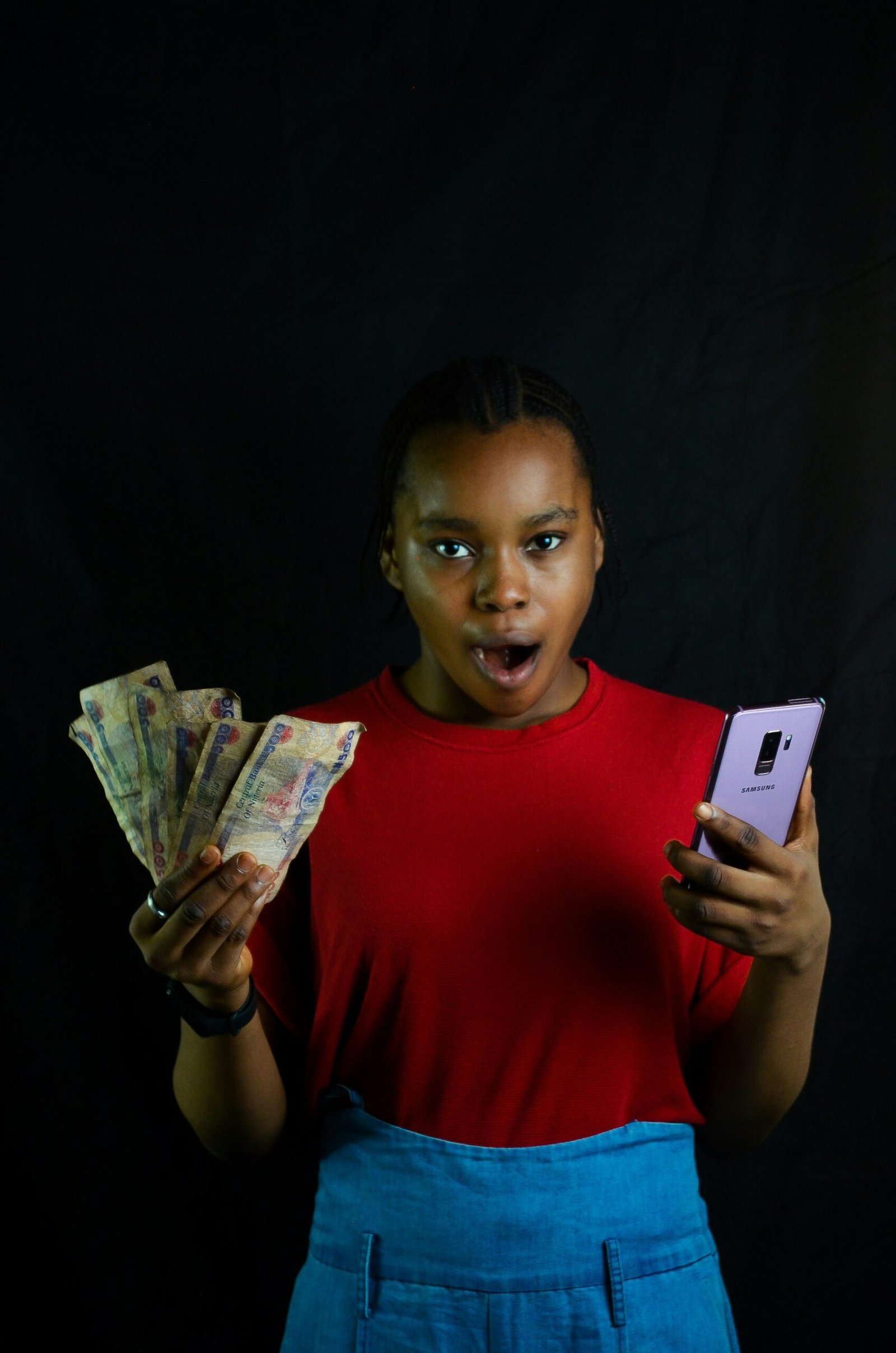 uma jovem negra com notas de dinheiro numa mão e o celular na outra