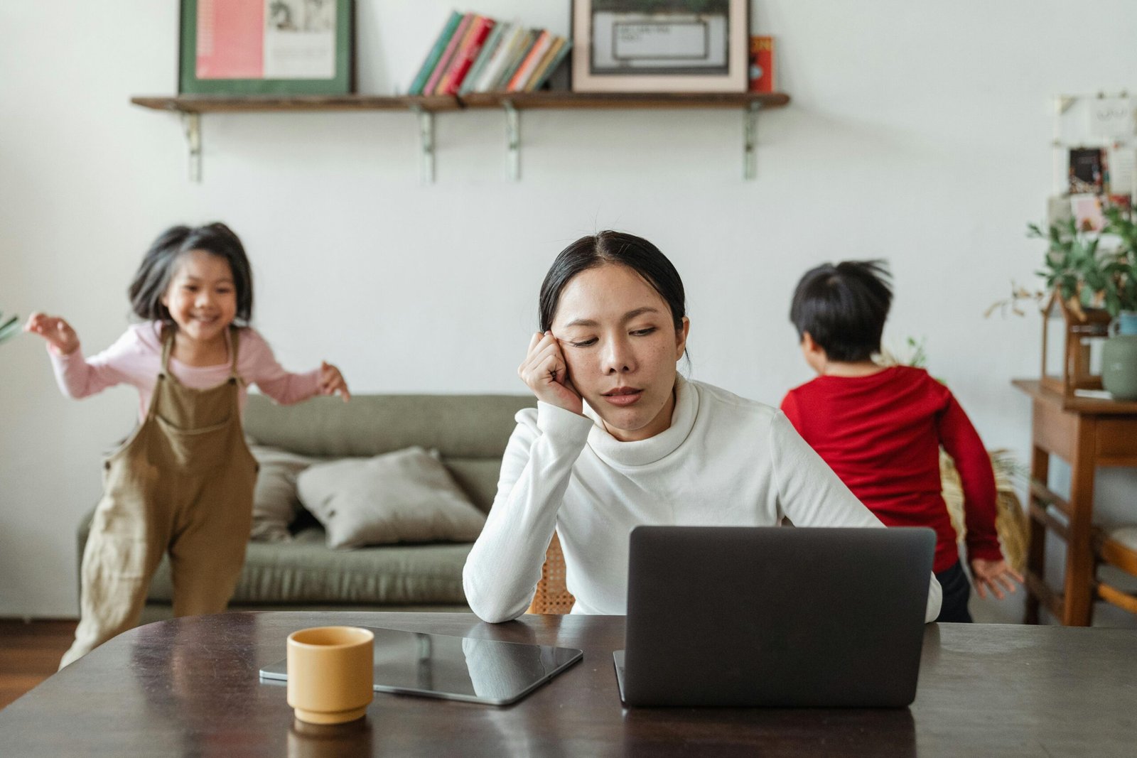 mulher em frente ao computador, trablhando em home office e seus dois filhos correndo pela sala