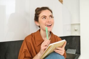 retrato-de-jovem-sorridente-com-pensamentos-criativos-olhando-para-cima-com-rosto-inspirado-segurando-caneta e caderno